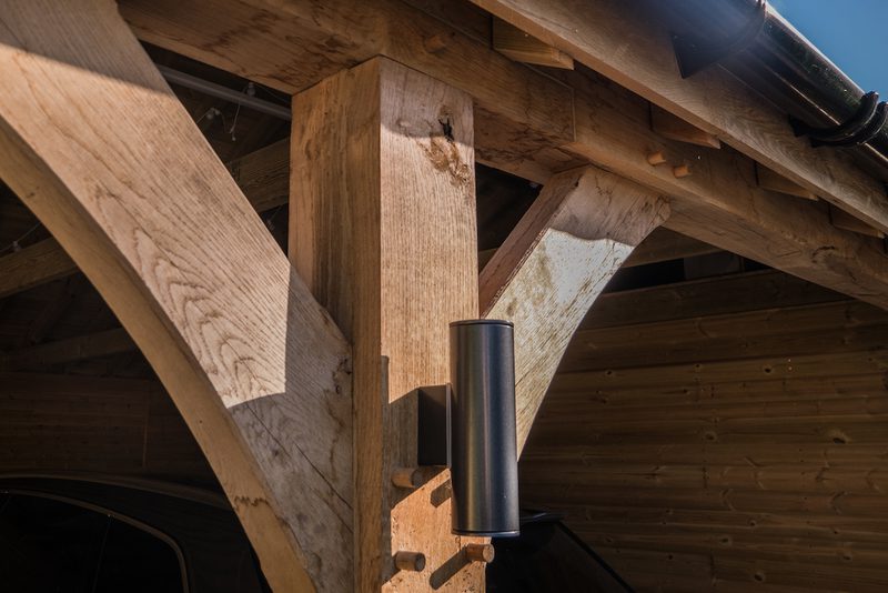 Close-up of timber roof framing with diagonal braces, featuring a black cylindrical device mounted on a vertical post beneath the eaves.