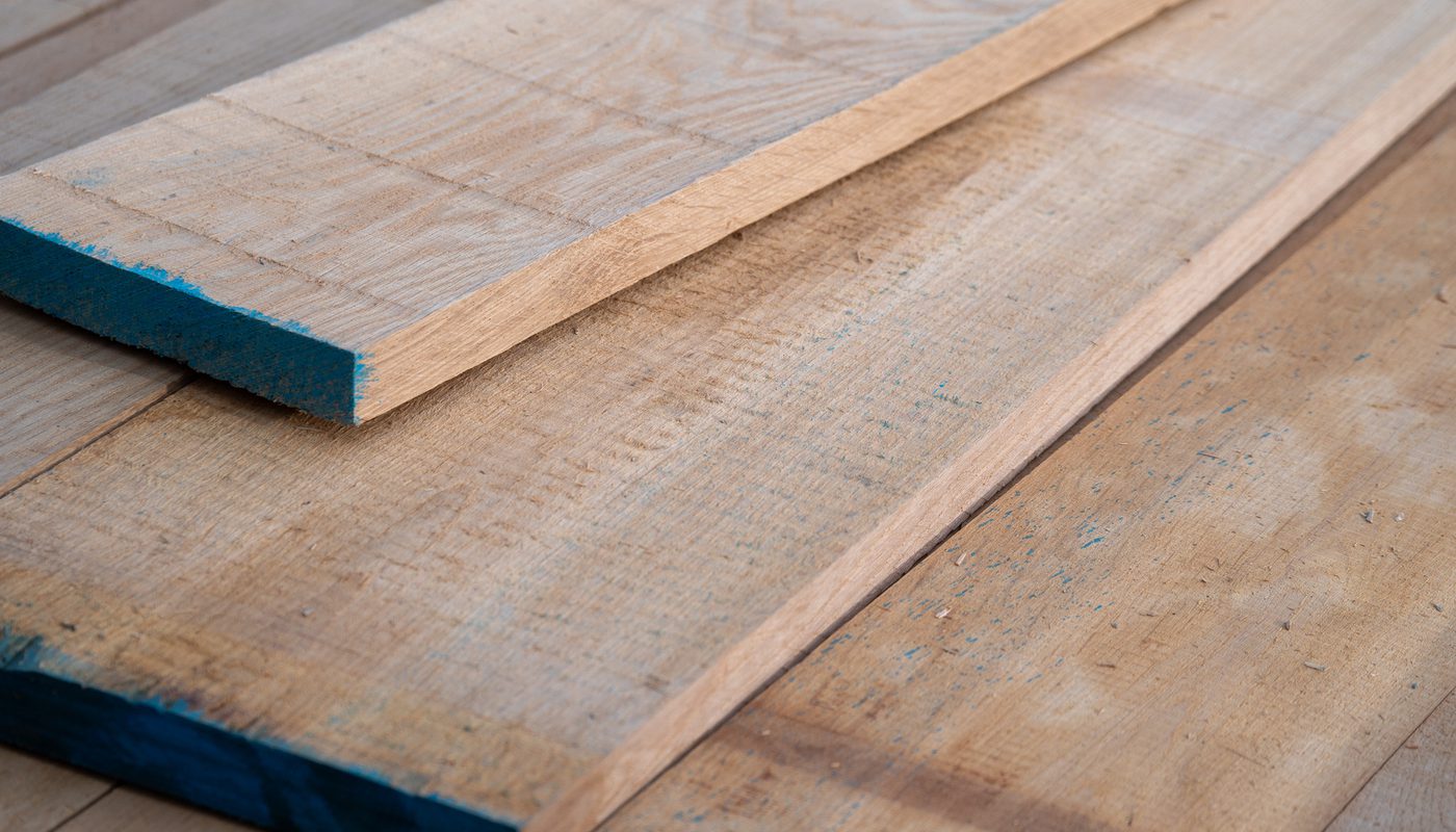 Close-up of weathered wooden boards with a narrow plank resting on top; blue paint on the ends and edges of the plank.