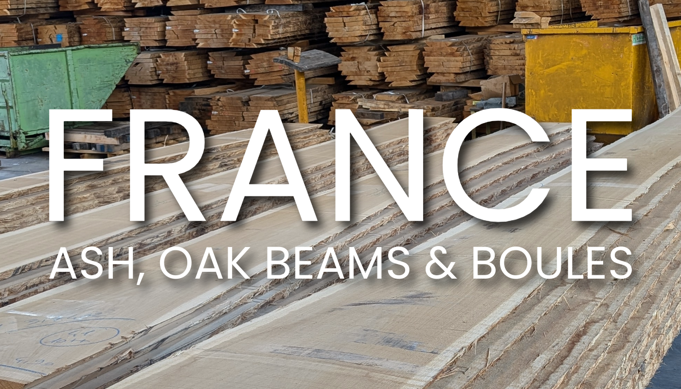 White text reads FRANCE and ASH, OAK BEAMS & BOULES over stacks of wooden beams in a lumber yard; green and yellow bins nearby.
