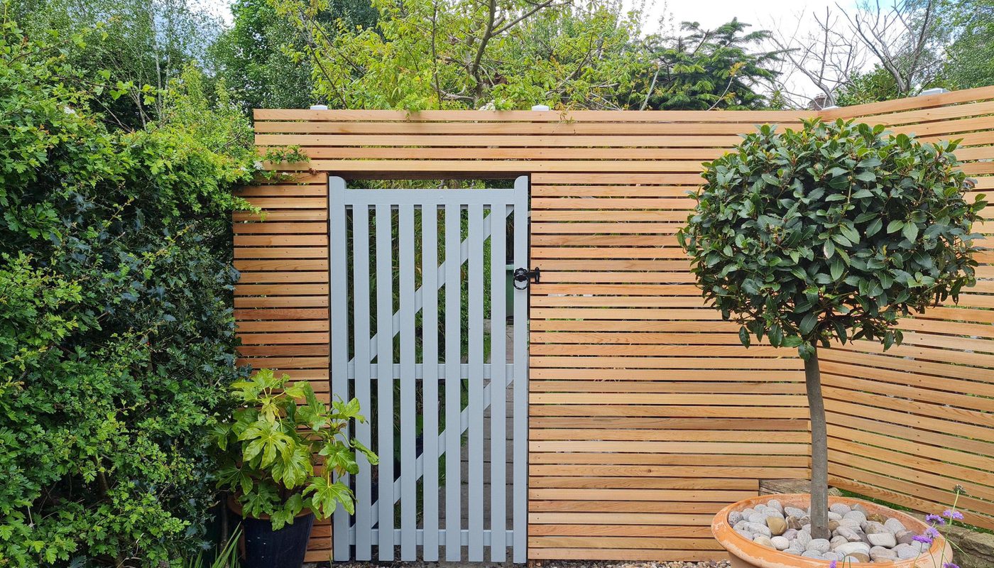 A designer garden with a wooden gate, greenery and slatted timber fence made of western red cedar.