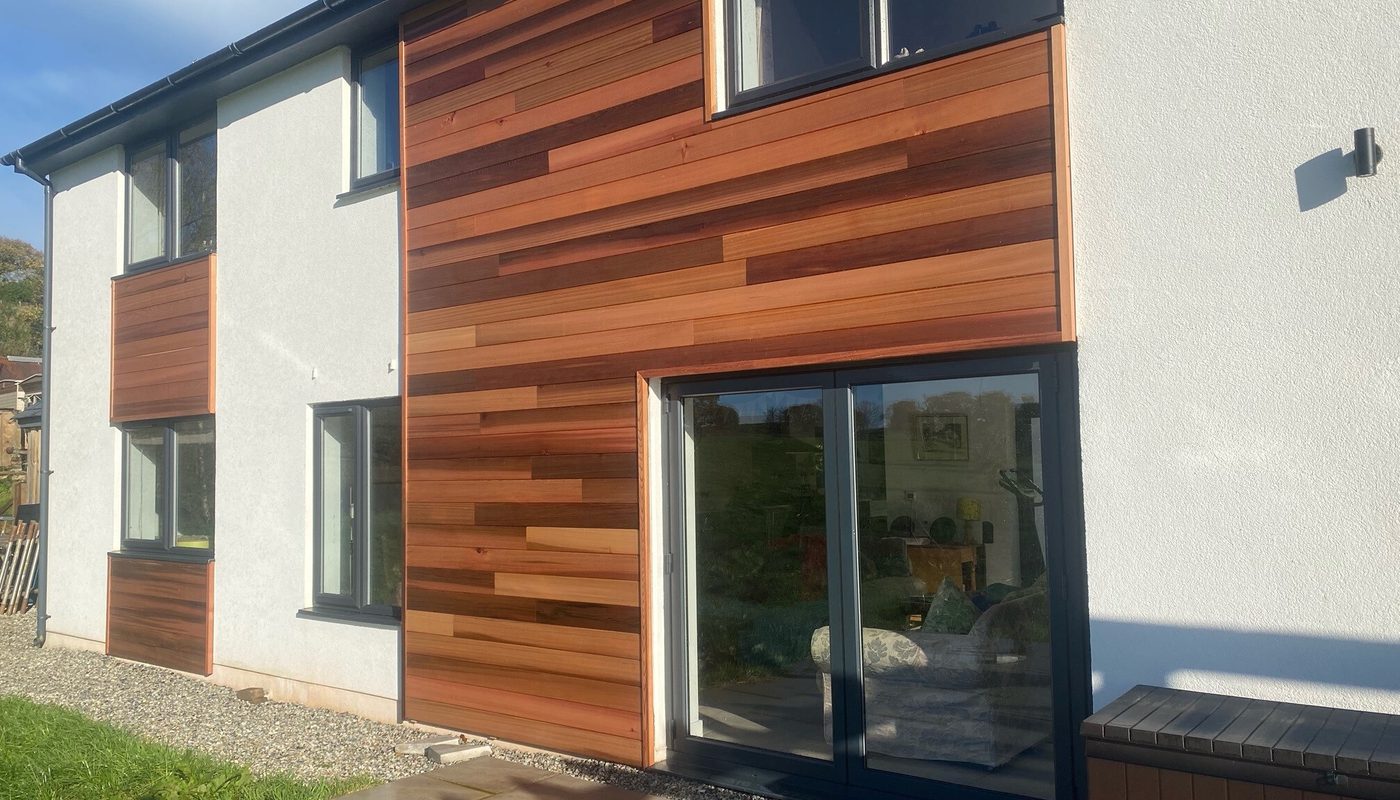 Modern two-story home with white walls and warm brown horizontal wooden cladding; large glass doors with dark frames.