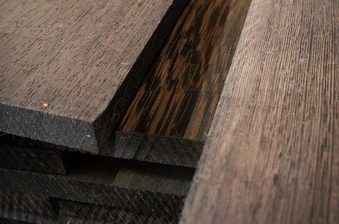 Close-up of dark-stained wooden boards stacked together, showing distinct grain patterns, beveled edges, and layered thicknesses.