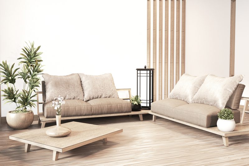 Bright minimalist living room with two beige sofas, a low wooden coffee table, potted plants, and a wooden slat divider.