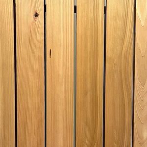 Close-up of vertical wooden planks with visible grain and knots, warm honey-brown color, and narrow gaps between boards.