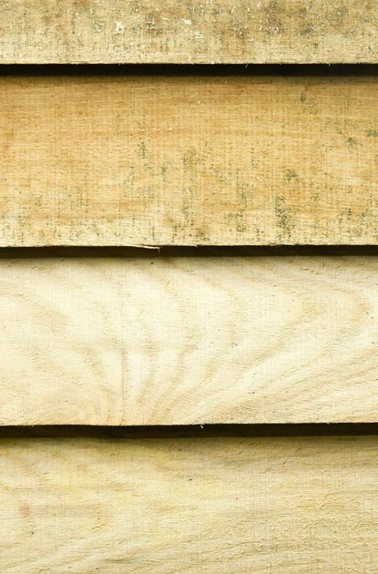 Close-up of horizontal wooden planks in beige tones, showing weathered grain and small gaps between overlapping boards.